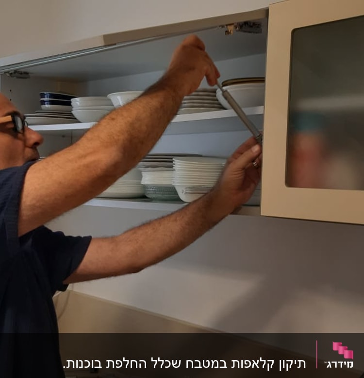 אדם מתקין דלת ארון מטבח עם כלים